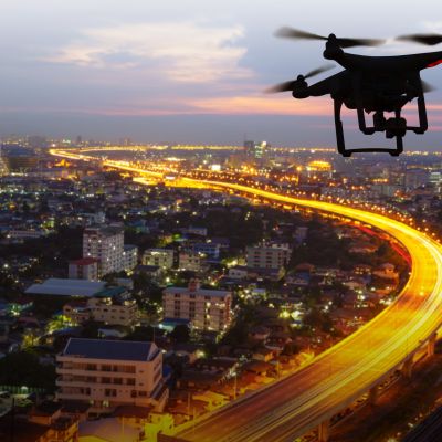Silhouette of drone flying above city at sunset